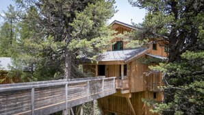 A treehouse with a wooden deck and a small porch, surrounded by dense forest.