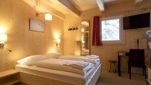 A wooden room with a bed, a desk, a chair, a mirror, and a TV.