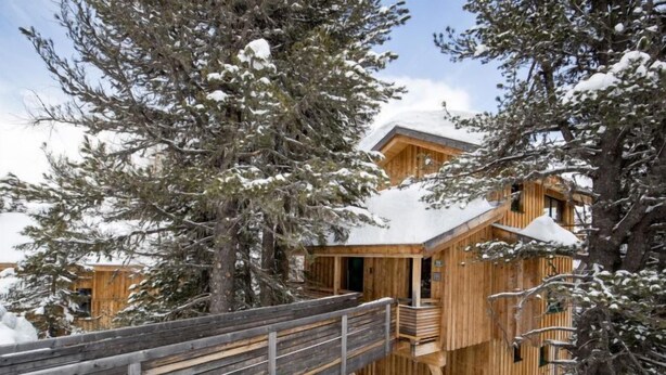 A wooden cabin with a wooden deck and a snow-covered roof.