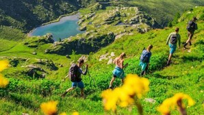 A group of hikers on a grassy mountain trail with a lake in the background.