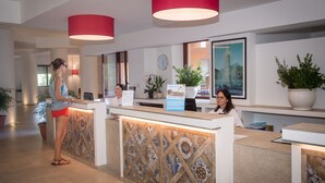 A reception area with a tiled wall, two receptionists, a clock, and potted plants. - Albergo Terme Sant'Egidio (Castelforte)