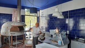 A kitchen with a pizza oven, a counter with a coffee pot, and a window with a view of trees. - Albergo Terme Sant'Egidio (Castelforte)
