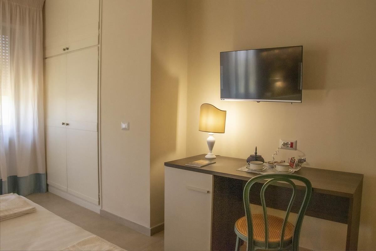 Habitación de hotel con cama, escritorio con lámpara, silla, televisor de pantalla plana y armario.