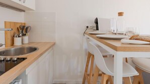 Une cuisine moderne avec des meubles blancs, un plan de travail en bois, un évier et un coin repas comprenant des chaises et une table, le tout dans des tons blancs.