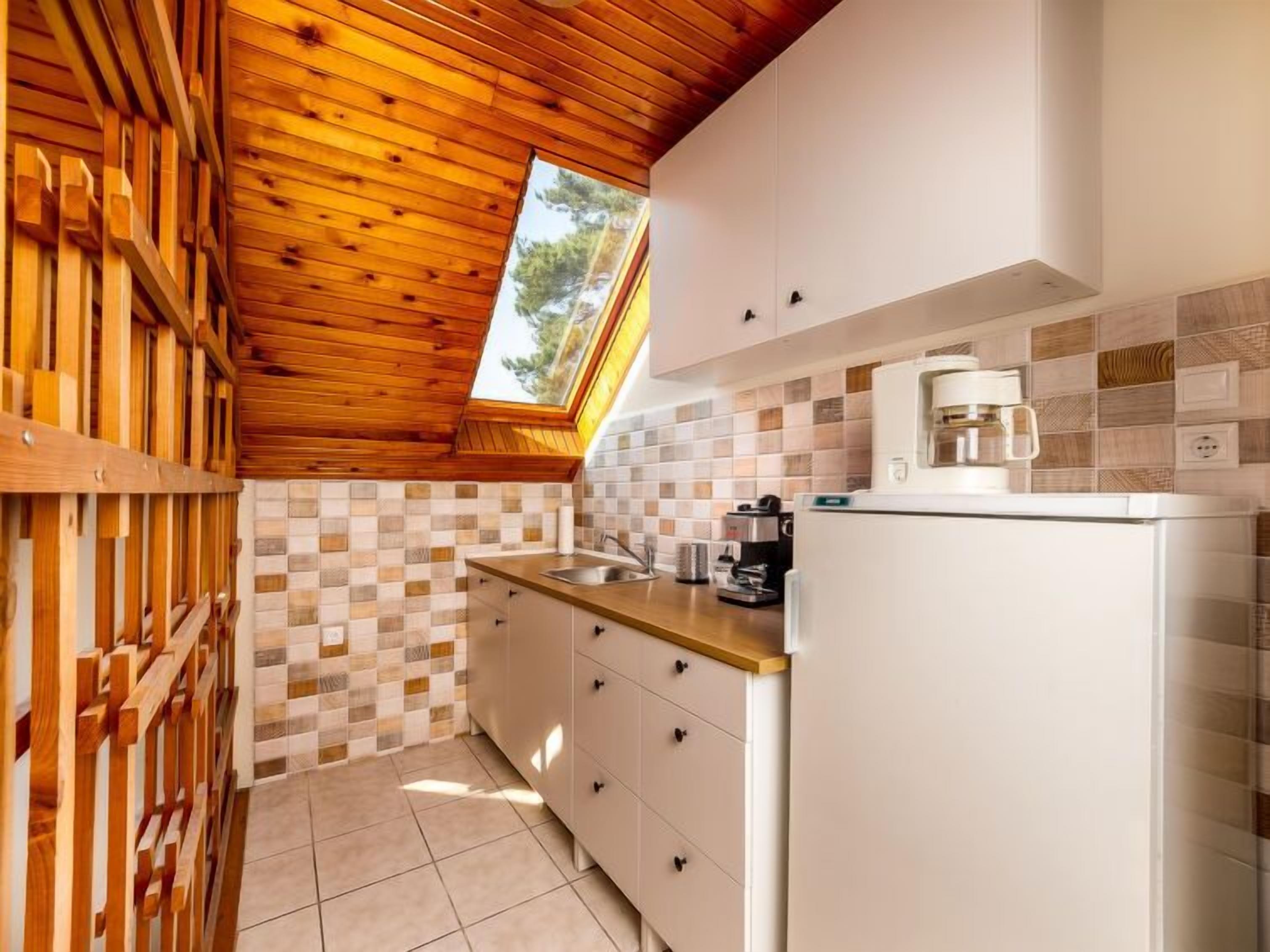 Una cocina compacta con vigas de techo de madera, un salpicadero de azulejos y un refrigerador empotrado.