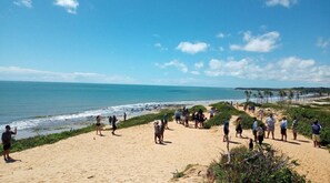 A beach with people walking and standing on the sand, overlooking the ocean. - Vida no Paraíso Lagoinha (Paraipaba)