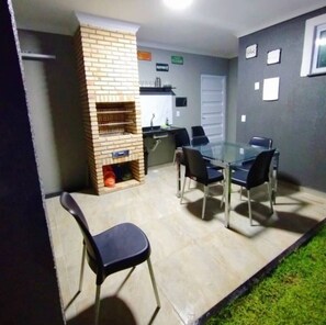 A meeting room with a glass table, black chairs, a brick fireplace, and a small kitchen area. - Vida no Paraíso Lagoinha (Paraipaba)