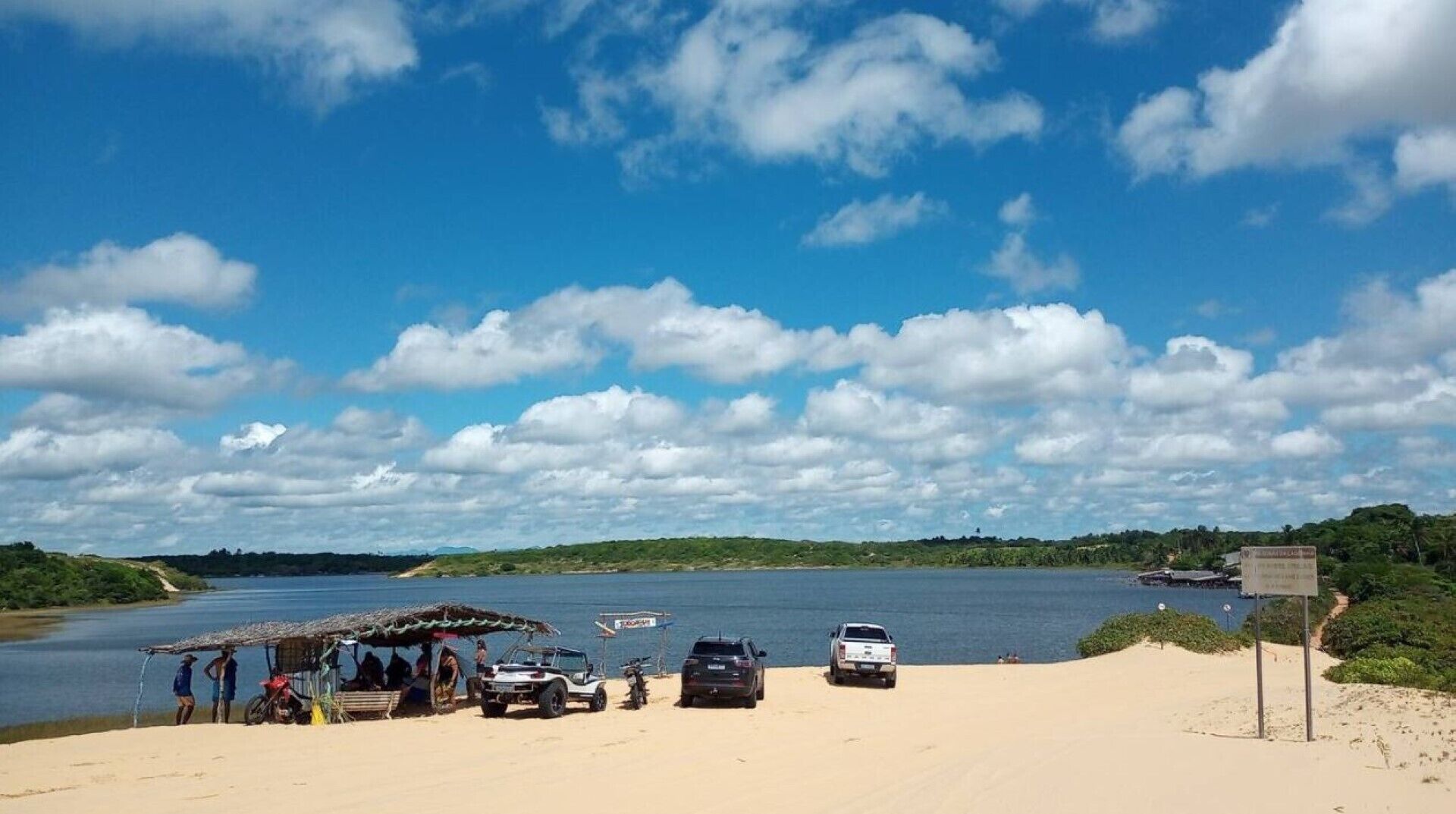Ein Strand mit einer kleinen Hütte, einigen geparkten Fahrzeugen und einem Schild.