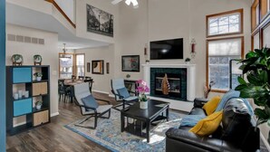 A spacious living room with a fireplace, a television mounted above it, and a dining area in the background. - Entire 3-level, 3 BRM home w/King/Queen/Twin beds (Topeka)
