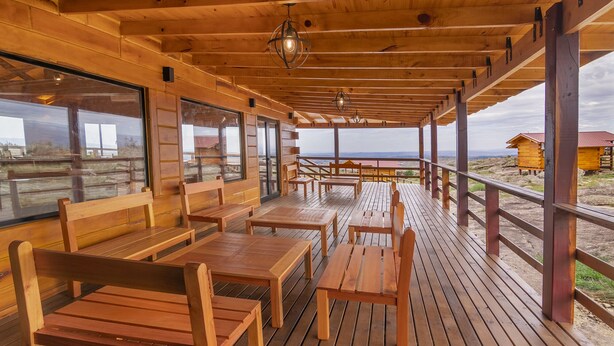 Een houten terras met banken en tafels, grote ramen en uitzicht op het landschap.