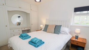 A neatly made bed with blue towels, a bedside lamp, and a window with a view. - Min Y Mor (Criccieth)
