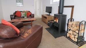 A cozy living room with a leather sofa, a coffee table, a TV, and a black wood-burning stove. - Min Y Mor (Criccieth)
