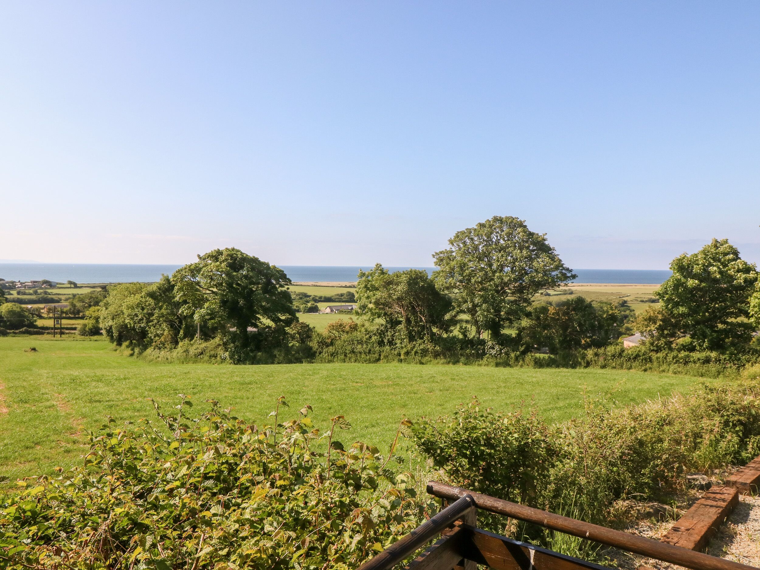 A rural landscape with a clear view of the sea, green fields, and scattered trees.