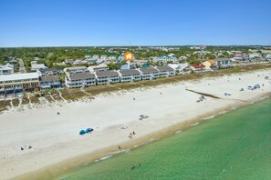 Oversigtsbillede af et kysthotelområde med ejendomme ved stranden, klart turkis vand og en sandstrand.