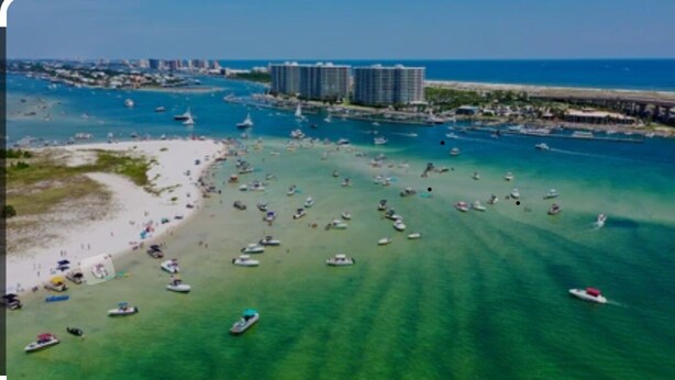 Vista aerea di una spiaggia con numerose imbarcazioni, un molo e grattacieli sullo sfondo.