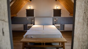 A room with a wooden ceiling, a bed with a white bedspread, two bedside tables with lamps, and a radiator on the wall.