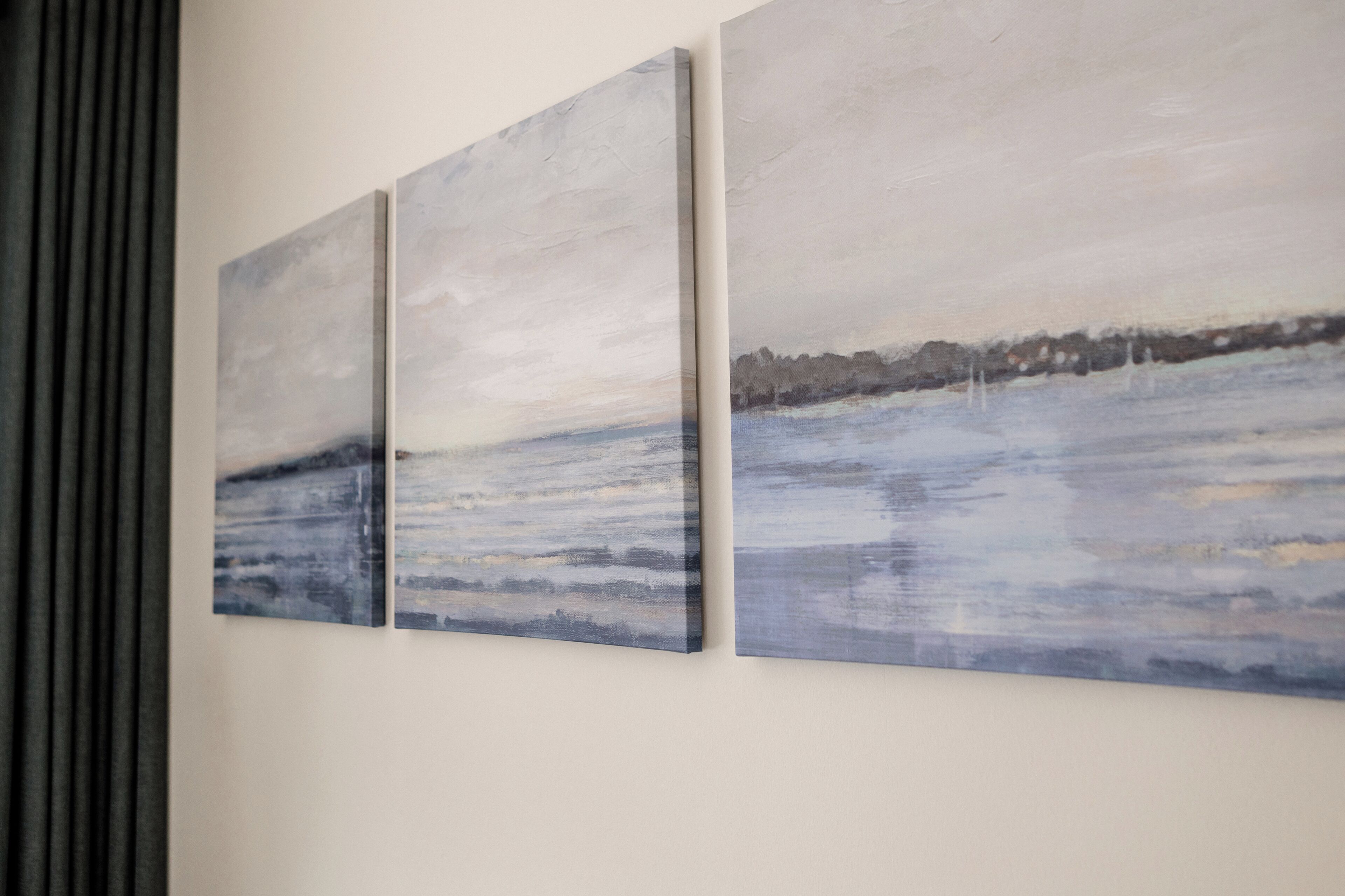 Drei an der Wand befestigte Gemälde, die eine friedliche Landschaft mit einem Gewässer und Bäumen zeigen.
