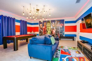 A room with a pool table, a blue sofa, and a colorful comic book-themed carpet.