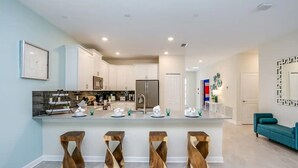 Una cocina moderna con armarios blancos, electrodomésticos de acero inoxidable y una isla central con taburetes.