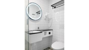Un baño moderno con un lavabo con mampara de vidrio, un espejo redondo con luz, un inodoro y un perchero para toallas.
