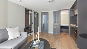 Una habitación de hotel moderna con un sofá gris, una mesa de centro con velas, un armario y una cama al fondo.