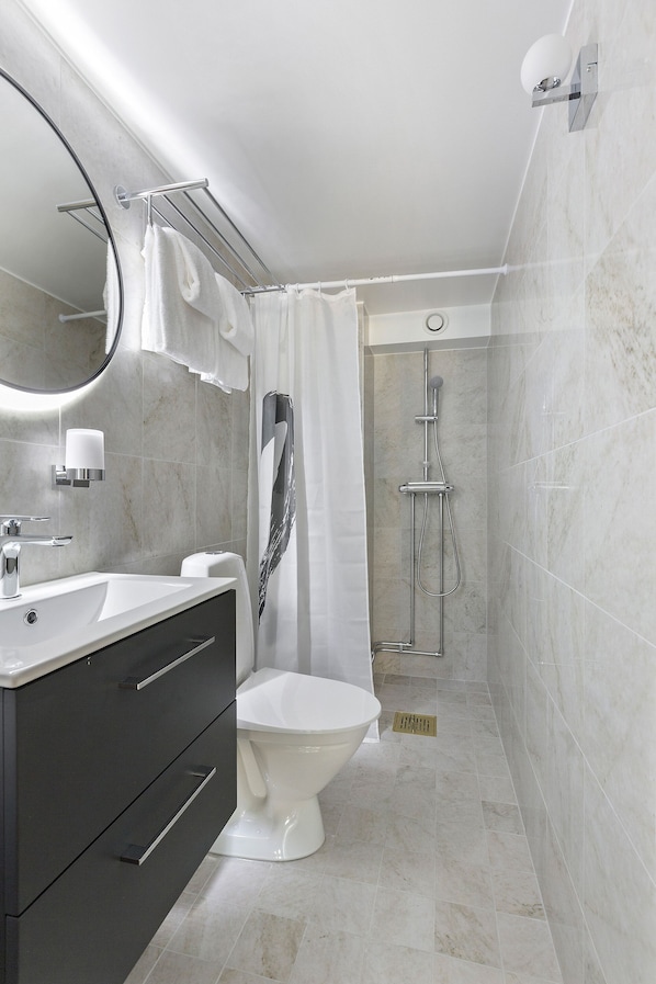 A modern bathroom with a white sink, dark vanity, toilet, and shower. - At Old Town Aparthotel (Stockholm)