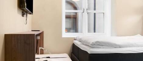A bedroom with a bed, a TV mounted on the wall, a window with a view, and a wooden dresser.