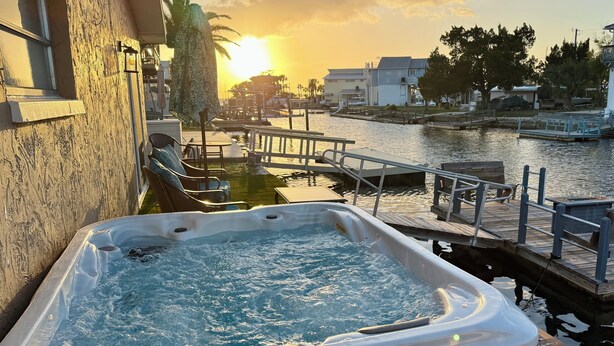 Ein Whirlpool mit Holzverkleidung, eine Anlegestelle und ein Sonnenuntergang über dem Wasser.