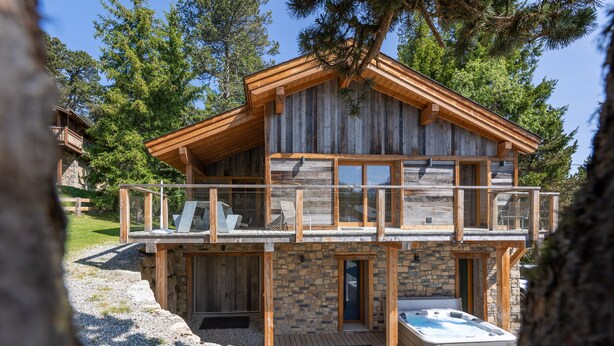 Eine Holzhütte mit Balkon, Steinwänden und einem Whirlpool.