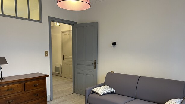Una habitación con un sofá gris, un aparador de madera y una puerta que da a otra habitación.