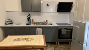Una cocina moderna con gabinetes grises, un refrigerador de acero inoxidable, un tostador, una cafetera y un suelo con estampado tipo espiga.