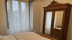 Un dormitorio con cama, armario de madera y ventana con cortinas traslúcidas.