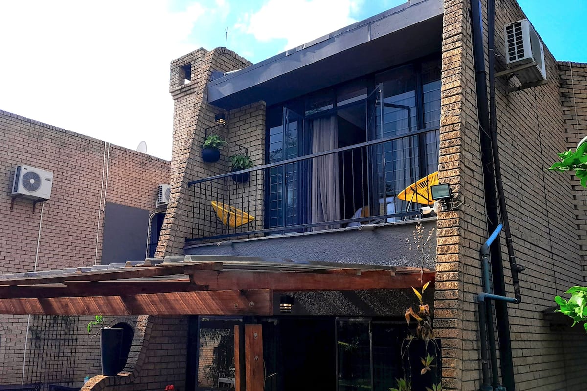A two-story brick building with a balcony, air conditioning units, and potted plants.