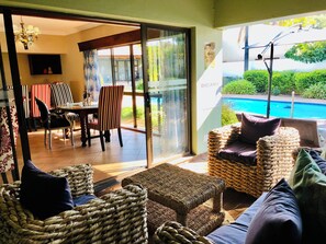 A room with a glass door leading to an outdoor area, a pool, and a dining setup with striped chairs. - Grafiti Boutique Hotel (Bela-Bela)