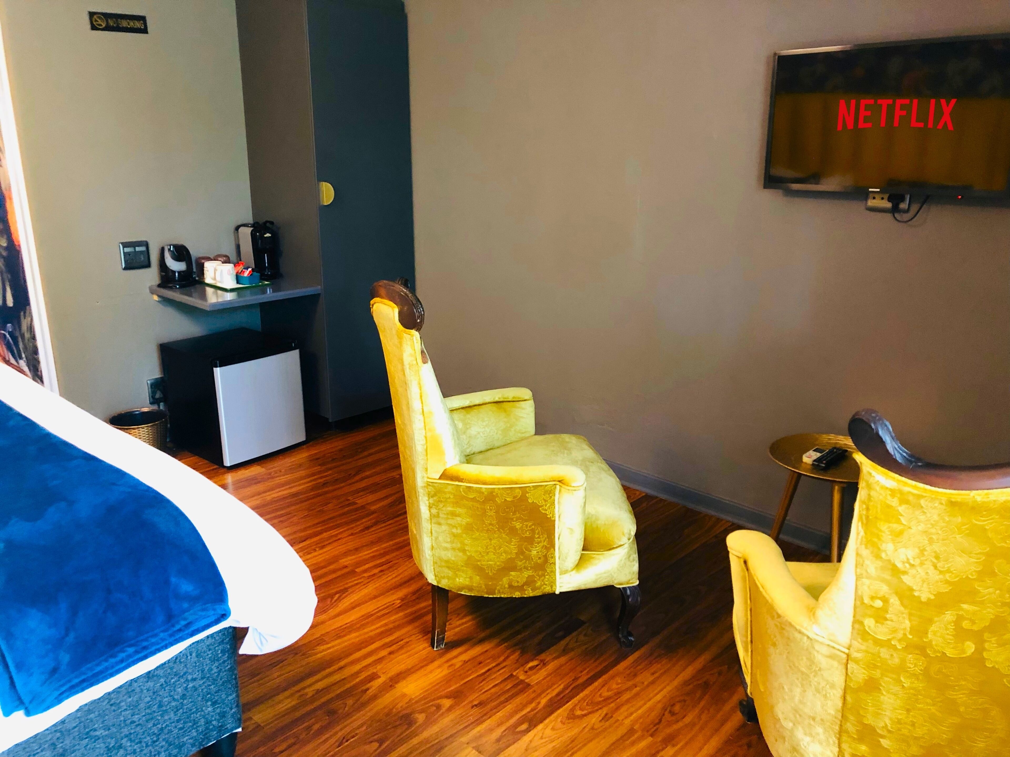 Une chambre d’hôtel avec un lit, un fauteuil jaune, une petite table, un téléviseur affichant le logo « NETFLIX » et un coin cuisine.