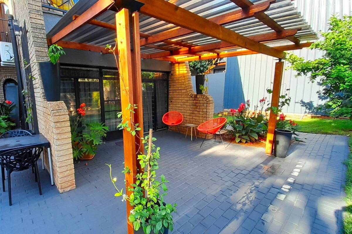 An outdoor patio area with a pergola, brick walls, potted plants, and outdoor furniture.