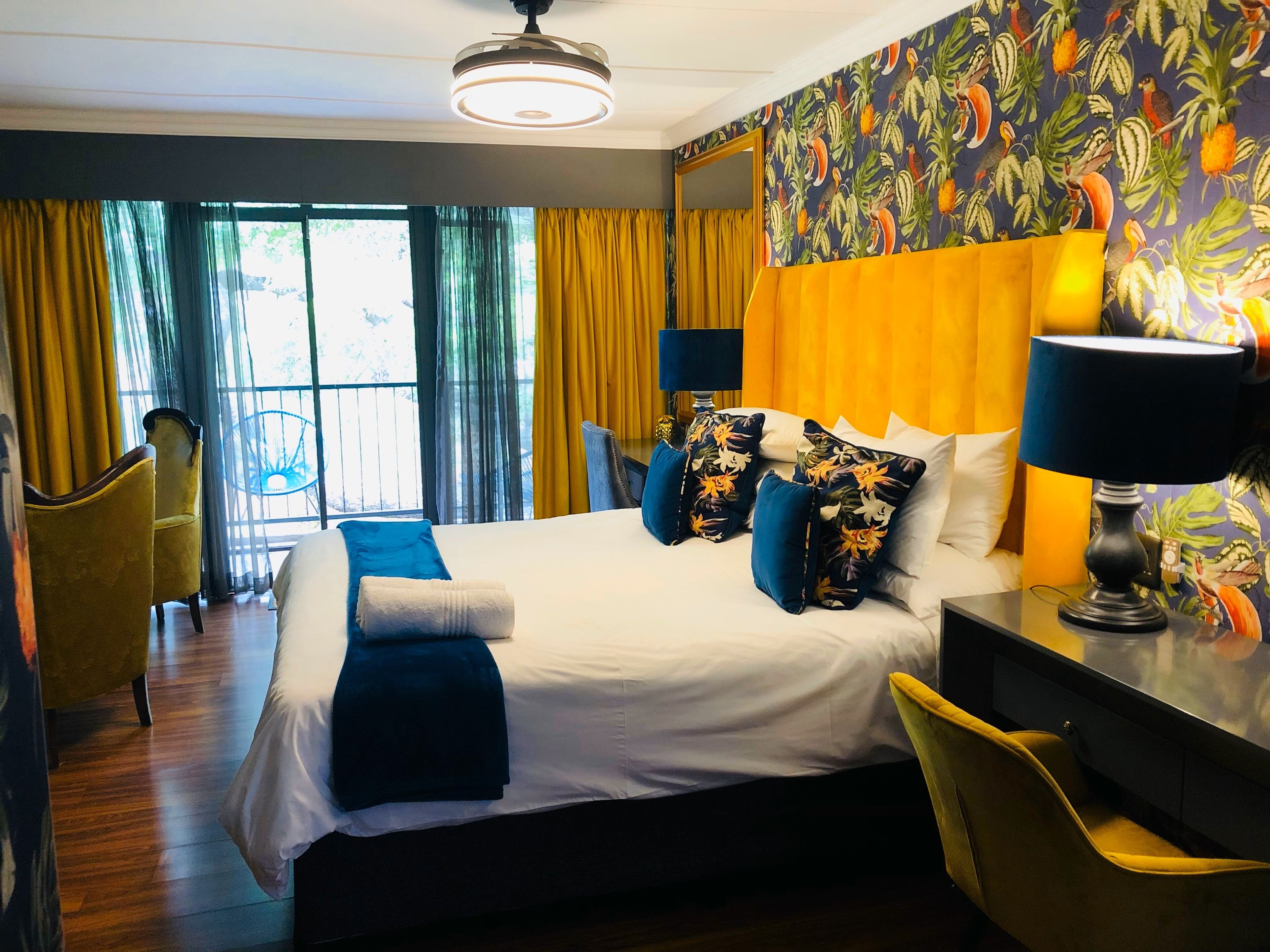Ein Hotelzimmer mit einem großen Bett, gelben Stühlen, einem Schreibtisch mit Lampe und einem fenster mit Vorhängen.