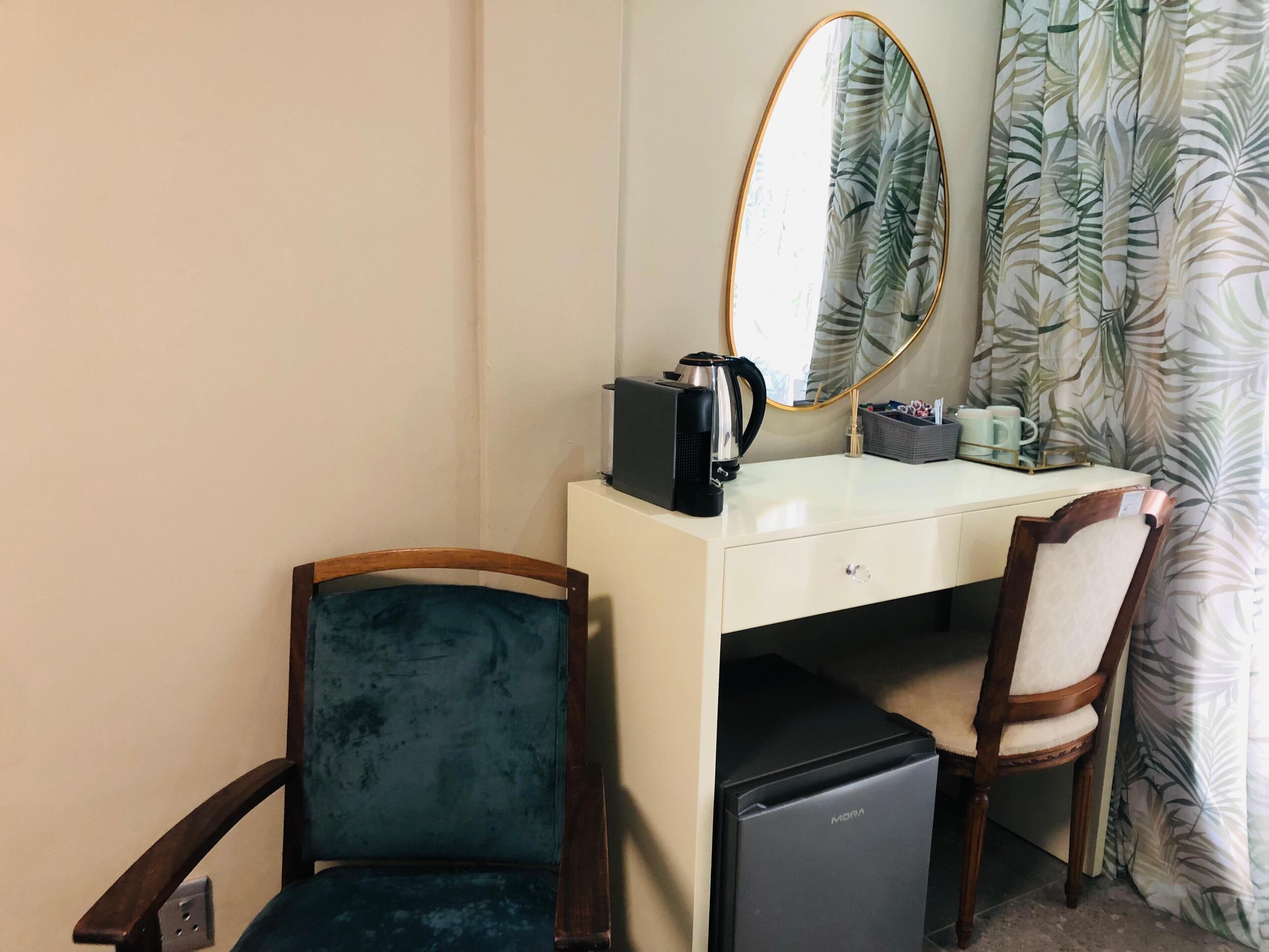 Une chambre d’hôtel de taille réduite, comprenant un petit bureau, une chaise, un mini-réfrigérateur, une machine à café et un miroir.