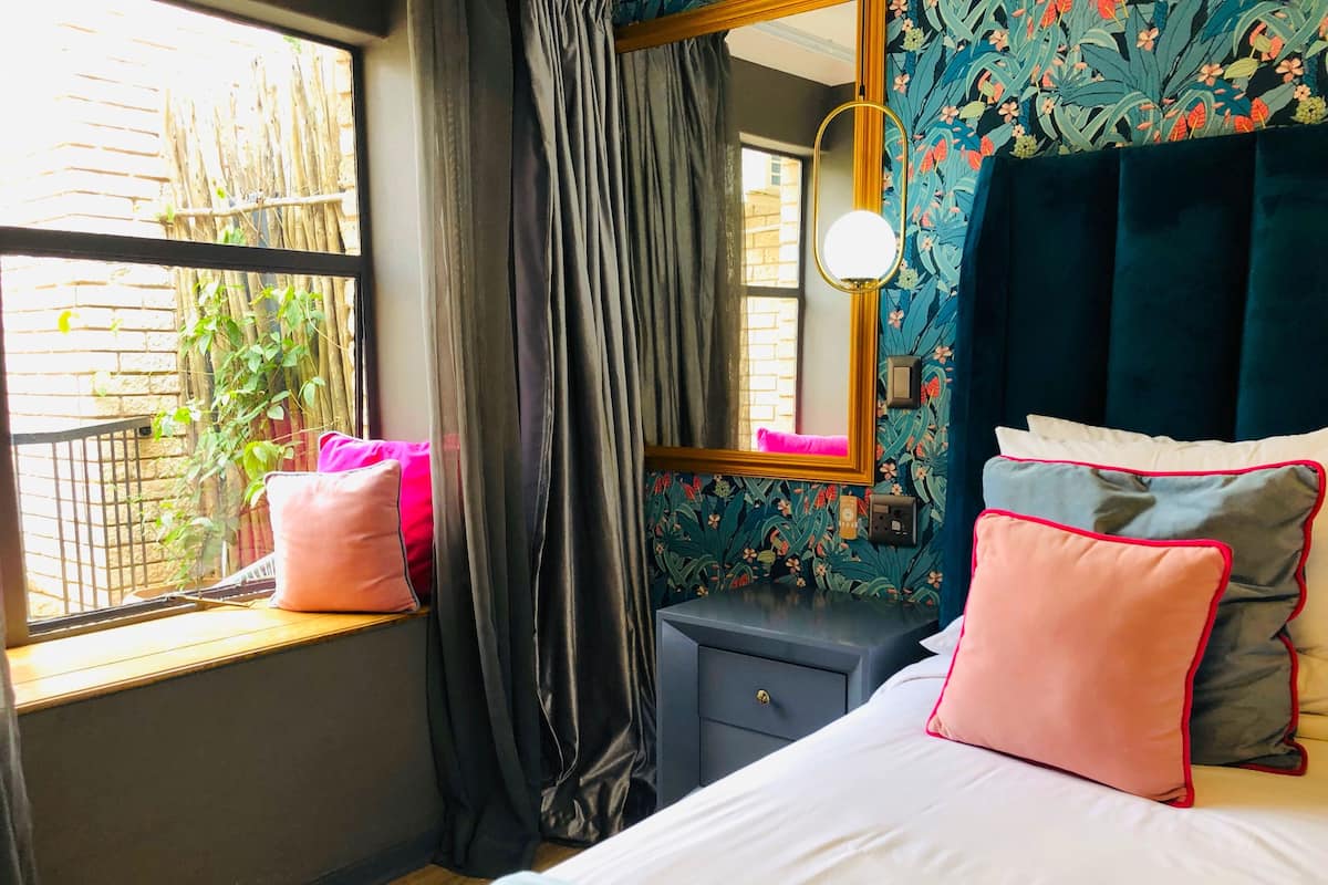 A bedroom with a bed, a bedside table, a mirror, and a window with curtains.