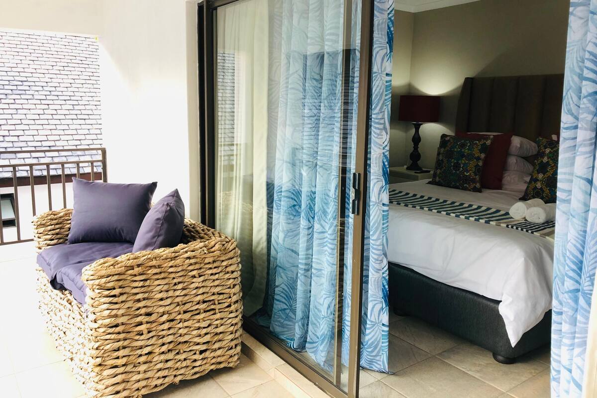 A room with a bed, a wicker chair, and a view through a glass door.