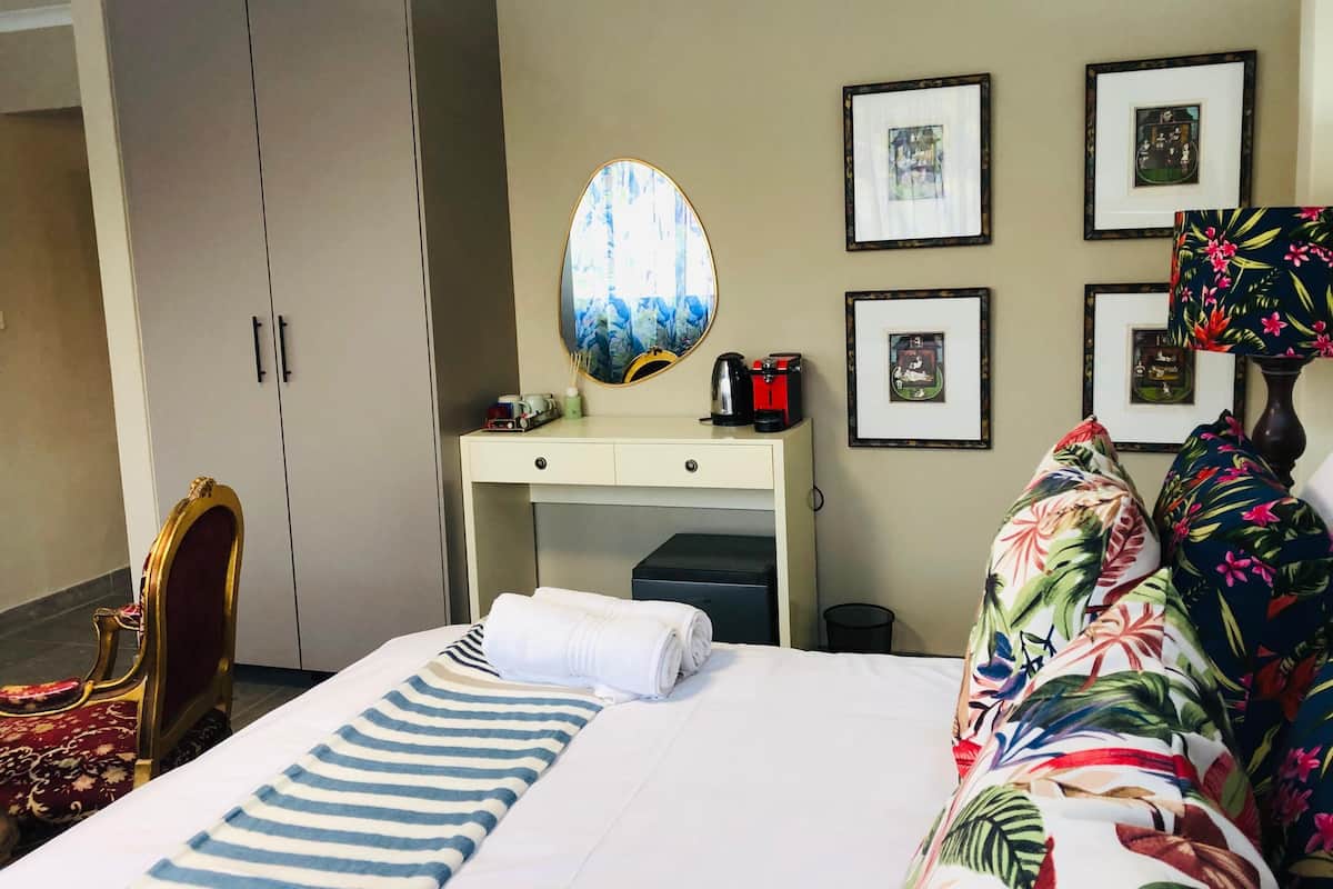 A hotel room with a bed, a desk with a mirror, a wardrobe, and framed pictures on the wall.