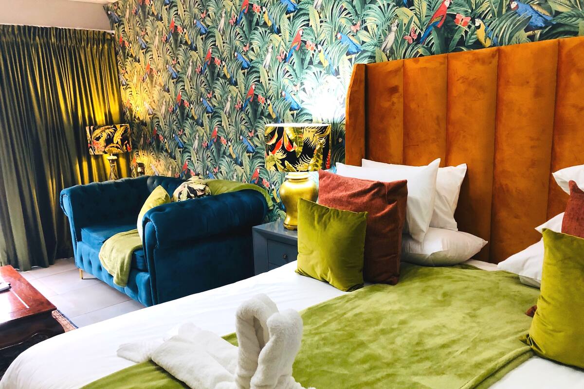 A hotel room with a large bed, two blue sofas, a colorful mural, and a wooden headboard.