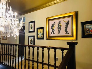 Una escalera con barandilla de madera, un candelabro y cuadros en la pared.
