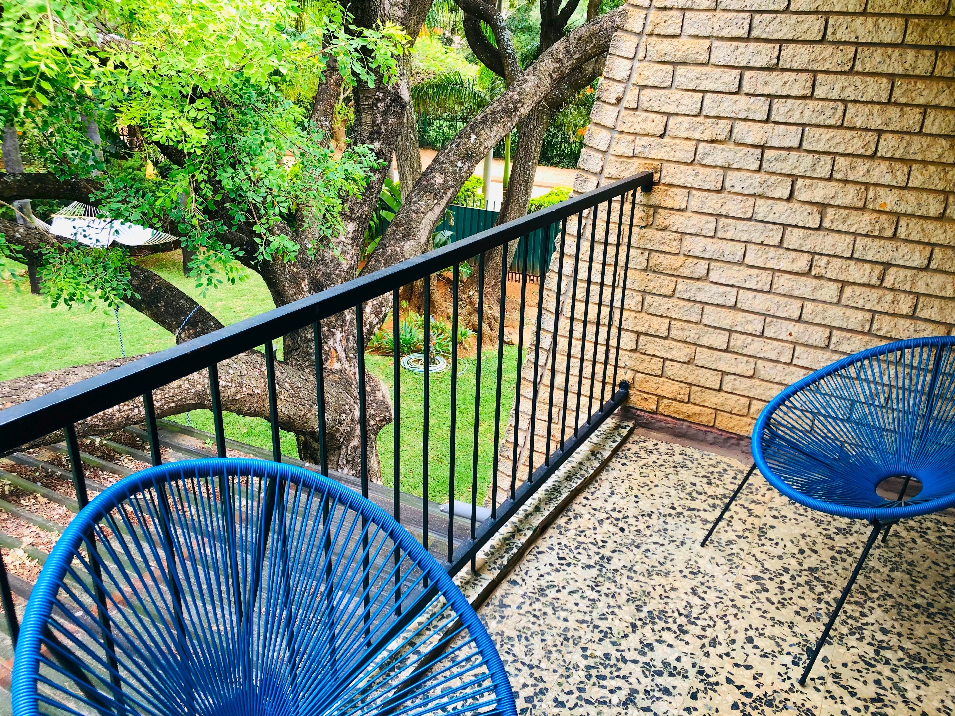A balcony with a brick wall, a metal railing, and two blue chairs.