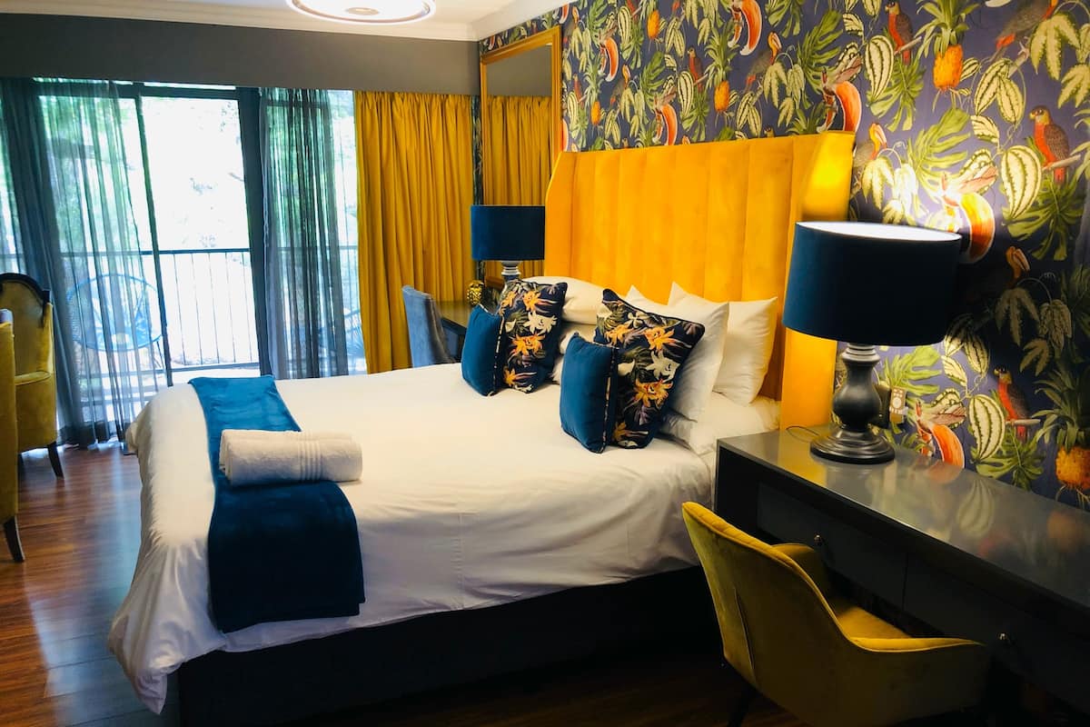 A hotel room with a large bed, a desk, and a chair. There is a window with curtains and a view of trees.