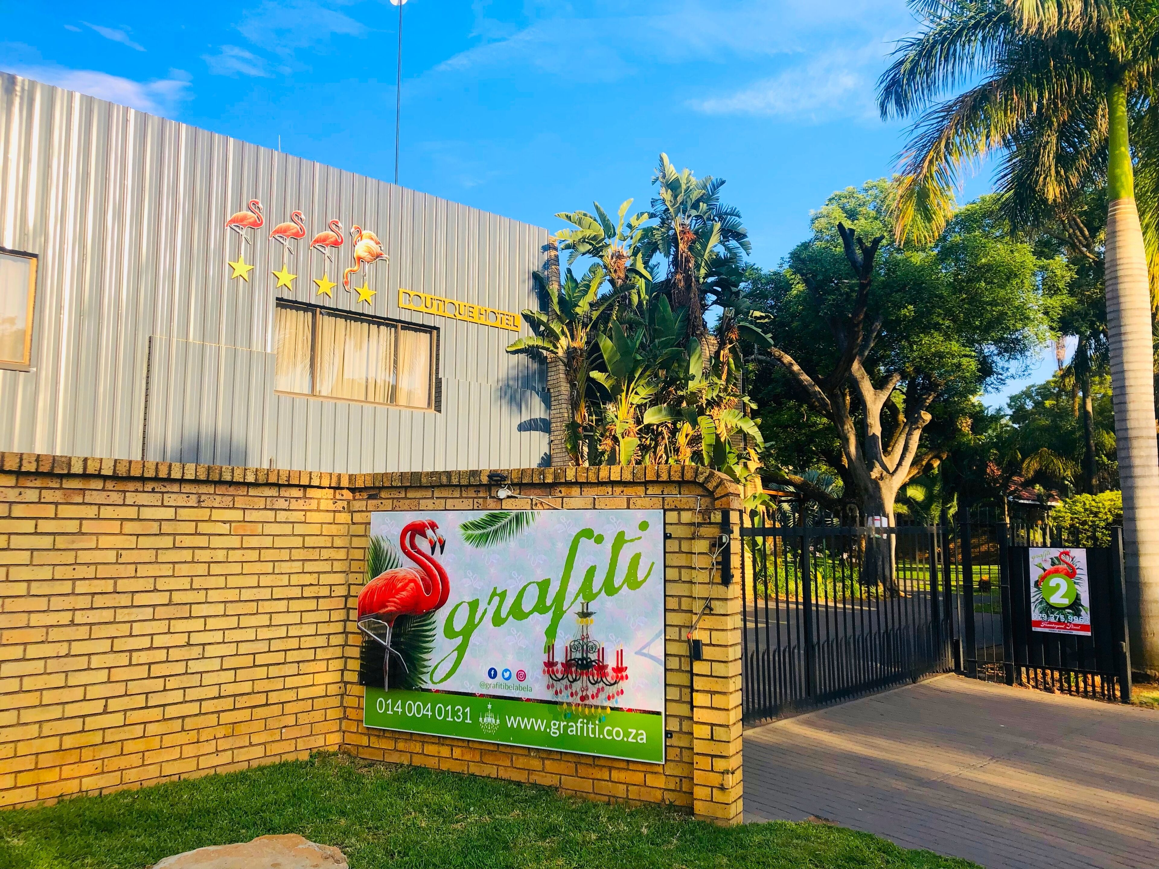 A hotel with a corrugated metal facade and a brick lower section. There is a sign for 'Boutique Hotel' and a large 'Grafiti' advertisement featuring a flamingo.