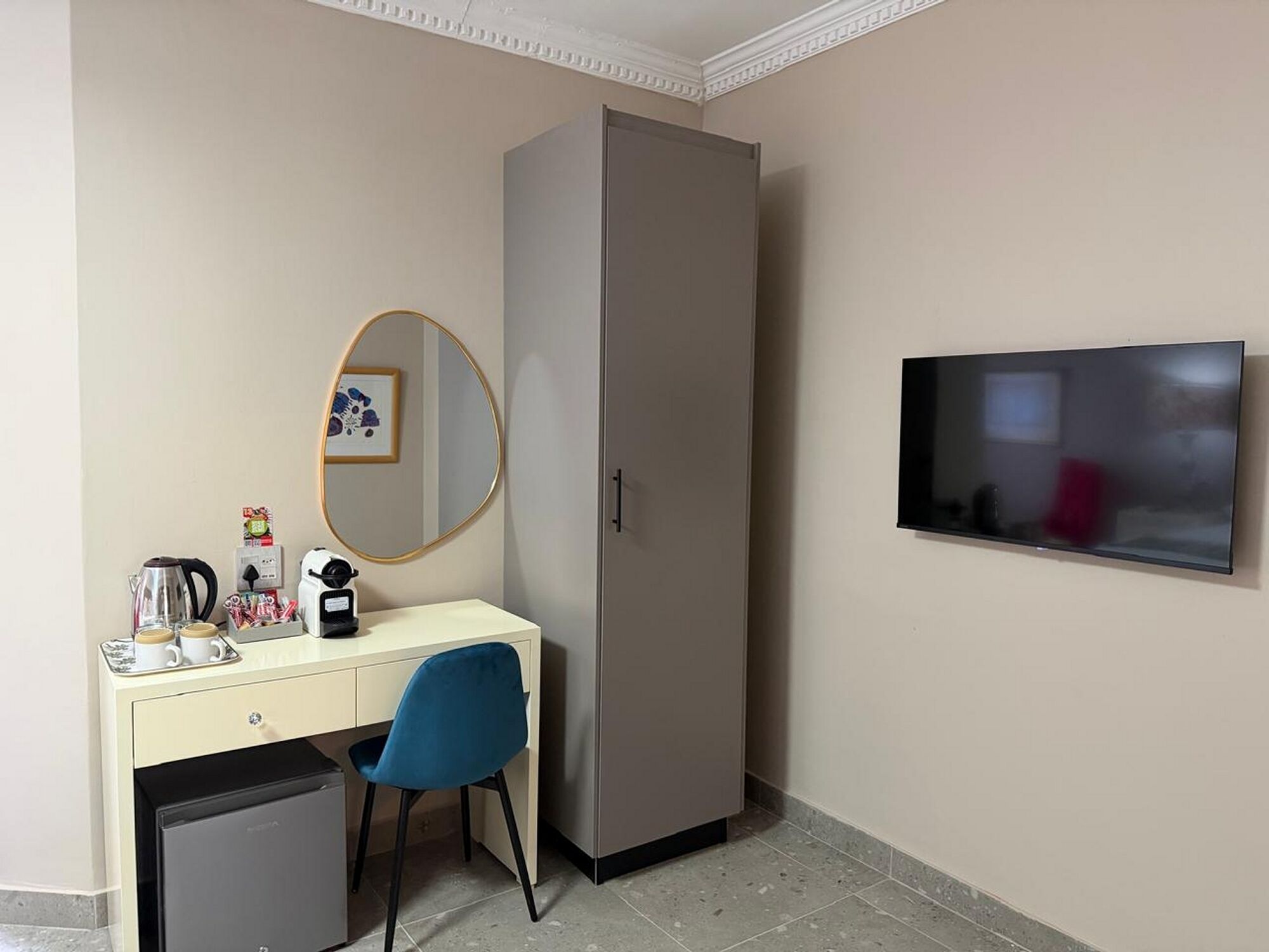 Une chambre d’hôtel compacte comprenant un bureau, une chaise, une armoire et un téléviseur fixé au mur.