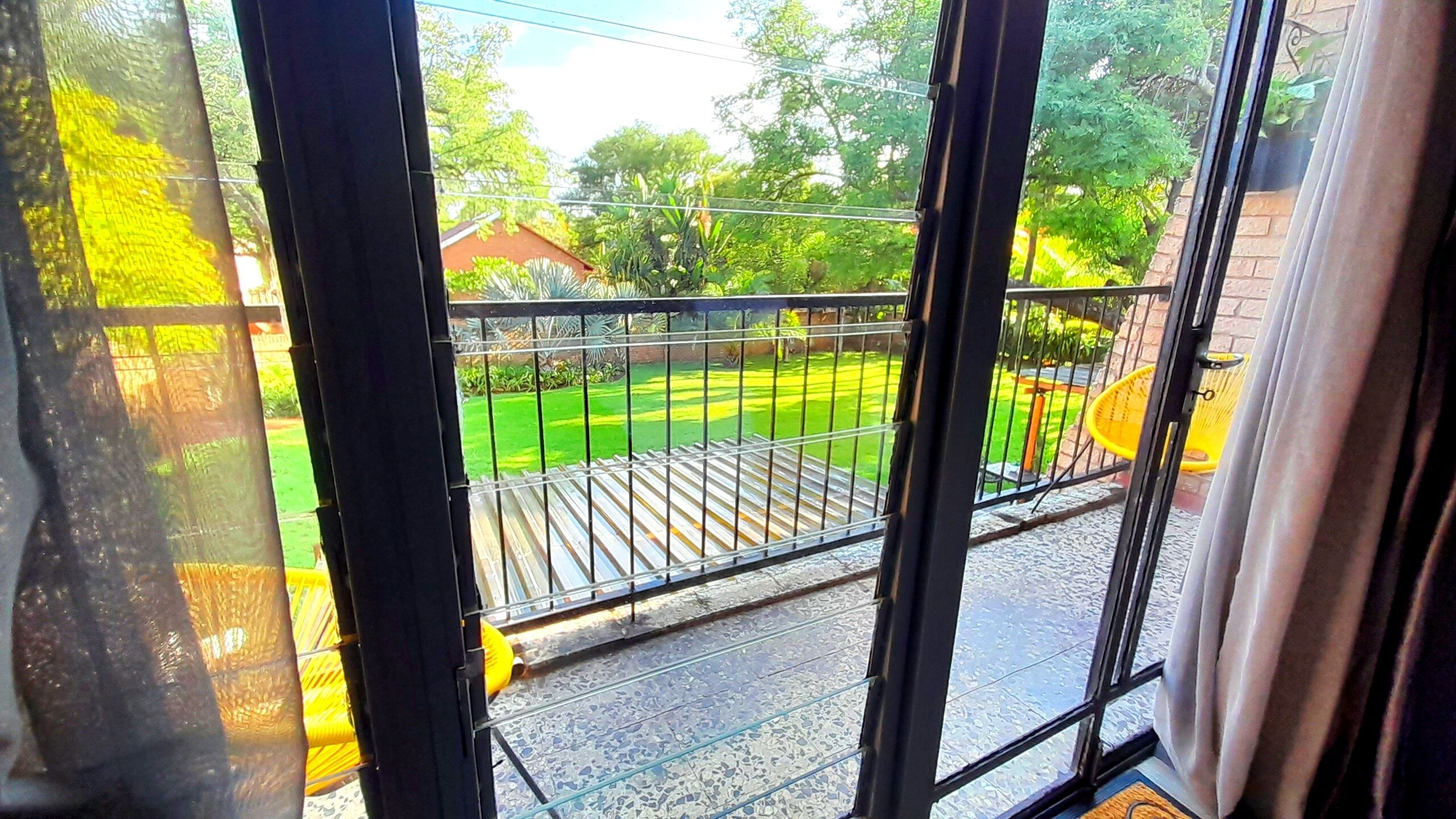 A view from a window with a metal railing overlooking a green lawn and a brick building.