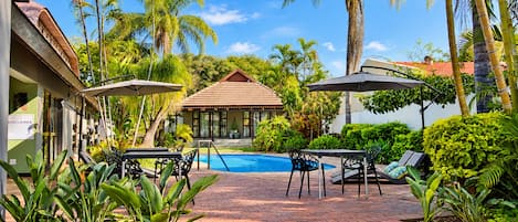 A pool area with a tiled deck, lounge chairs, and umbrellas.