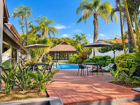 A pool area with a tiled deck, lounge chairs, and umbrellas.